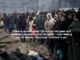 Refugees standing in a long line outdoors.