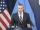 Official delivering statement at podium with flags