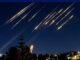 Lights streaking across night sky over city.