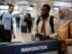 People at immigration counter with officer pointing.