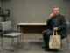 Man with bag sitting in empty room.