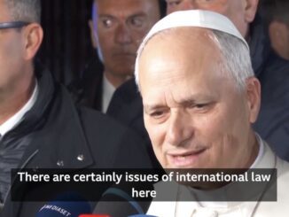 Man in white skullcap speaking to reporters