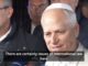 Man in white skullcap speaking to reporters