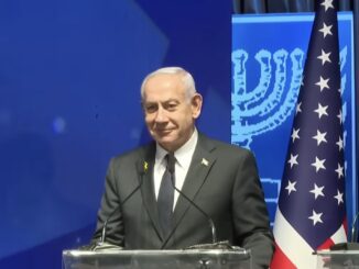 Smiling man in suit at podium with flags