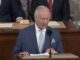 Elderly man in pinstripe suit speaking at podium
