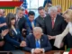 People praying around seated man at desk