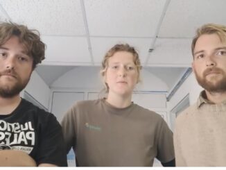 Three people standing indoors looking at camera