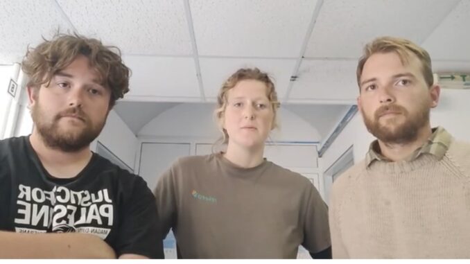 Three people standing indoors looking at camera Three people standing indoors looking at camera