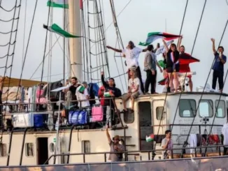 People waving flags aboard crowded sailboat deck