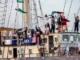 People waving flags aboard crowded sailboat deck