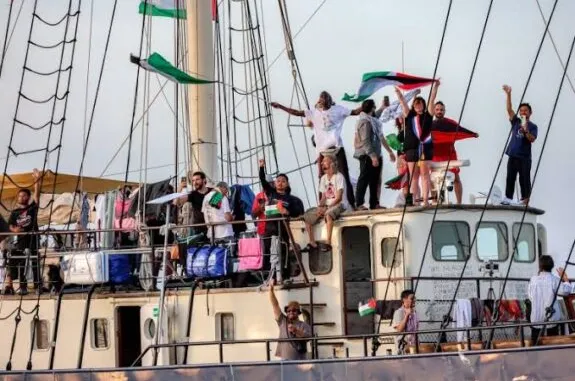 People waving flags aboard crowded sailboat deck