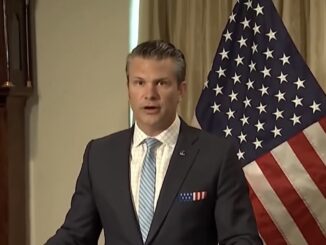 Man in suit speaking beside American flag