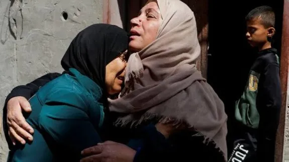 Two women embracing in grief, boy nearby Two women embracing in grief, boy nearby