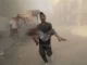 Man carrying child through dusty, rubble-strewn street