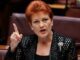 Red-haired woman pointing while speaking in chamber