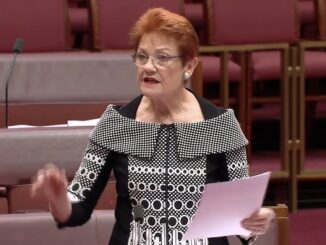 Woman speaking in parliamentary chamber holding paper