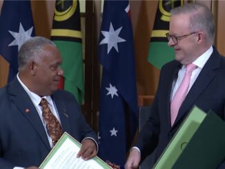 Two officials exchanging documents with flags backdrop