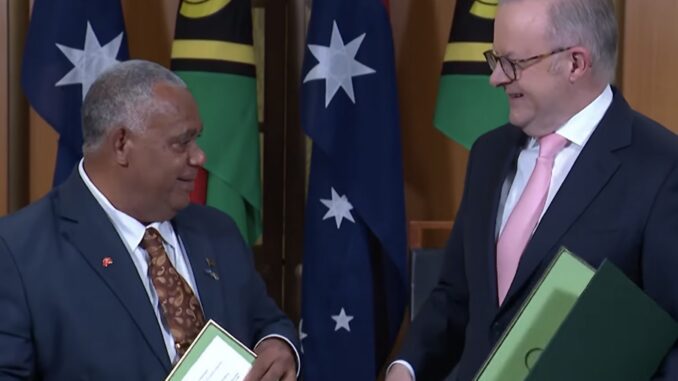 Two officials exchanging documents with flags backdrop