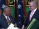 Two officials exchanging documents with flags backdrop