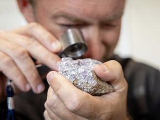Person examining rough mineral with jeweler's loupe