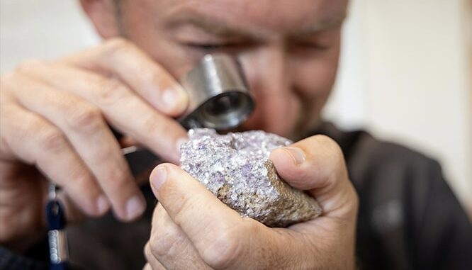 Person examining rough mineral with jeweler's loupe